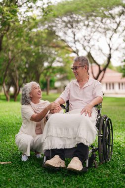 Yaşlı Asyalı çift parkta mutlu bir an yaşıyor. Kadın, tekerlekli sandalyedeki adama destek oluyor. İlişkisi var.