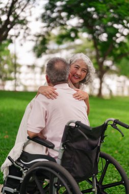 Asyalı yaşlı kadın tekerlekli sandalyede kocasına sarılıyor yeşil parkta emeklilik desteğini gösteriyor dışarıda mutluluk sağlık hizmetleri