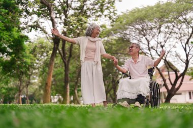 Mutlu yaşlı Asyalı çift tekerlekli sandalyede el ele tutuşup hayat ve arkadaşlık parkı kuruyor.