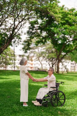 Emekli Asyalı çift, dışarıda uzun süreli bir sevgi bağı olduğunu gösteren el ele tutuşup destek buluyor..