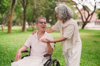 Asyalı yaşlı çift, emeklilik yıllarında tekerlekli sandalyedeki sevdiklerine yardımcı olmak için parkı paylaşmayı seviyor.