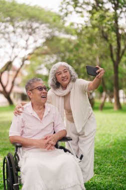 Mutlu Asyalı son sınıf çifti, emeklilik sırasındaki neşe ve bağlantılarını paylaşarak parkta mobil selfie çekmeyi seviyor.
