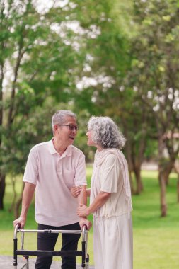 Asyalı yaşlı çift birlikte parkta gülümseyip sağlıklı bir hayat arkadaşı arıyor Walker 'ın emeklilik etkinliğini desteklemesine yardımcı oluyor.