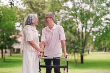 Mutlu Asyalı yaşlı çift emeklilikten sonraki altın yıllarda destekleyici ilişkiler gösteren yürüyüş yardımı kullanarak parkta geziniyor.