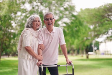 Asyalı yaşlı çift, parkta yürümeyi seviyor. Adam, Walker 'a yardım ediyor. Sağlıklı bir emeklilik öneriyor.
