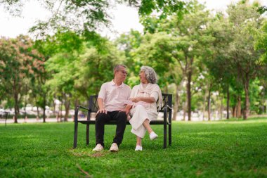 Yaşlı Asyalı çift parktaki bankta oturmuş sıcak havanın tadını çıkarıyor ve emeklilik sonrası sohbet ediyorlar.