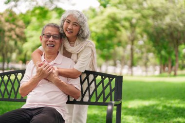 Mutlu yaşlı Asyalı çift rahatla. Park bankı kucaklaş. Huzurlu bir anı paylaş.