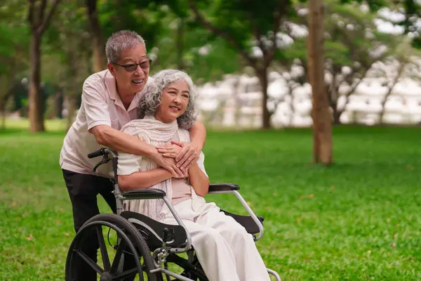 Park 'taki mutlu Asyalı yaşlı çift, emekli olduktan sonraki altın yıllarında tekerlekli sandalyedeki kadını kucaklıyor.