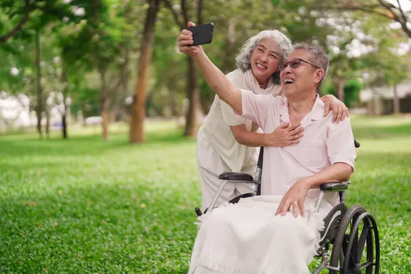 Mutlu Asyalı son sınıf çifti dışarıda fotoğraf çekmekten zevk alıyor. Tekerlekli sandalye partneri kullan.