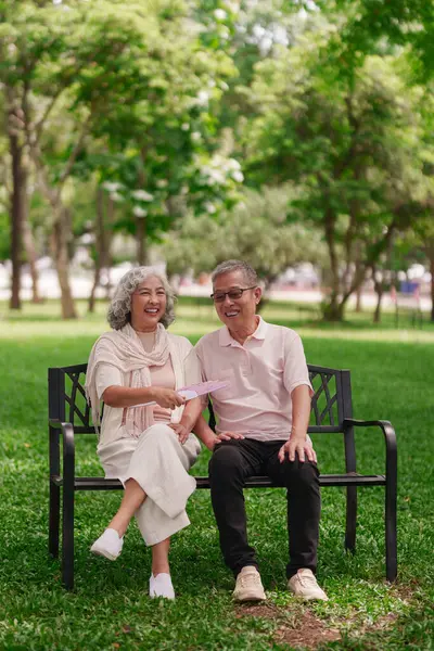 Mutlu emekli Asyalı çift bankta otururken sıcak park melteminin tadını çıkarıyor.