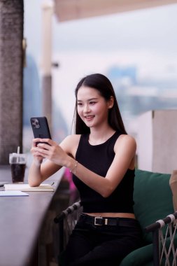 Kendine güvenen Asyalı yetişkin şık çatı katındaki bir salondan mobil bir cihaz kullanarak küresel olarak bağlantı kuruyor. Modern profesyonel başarıyı sembolize ediyor..