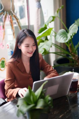 Kendine güvenen Asyalı kadın, profesyonel gelişim ve çevrimiçi ağ kurmak için şık bir kahve dükkanında taşınabilir bilgisayarında etkili bir şekilde çalışıyor.