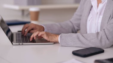 Yetişkin eller modern bir dizüstü bilgisayarı etkin bir şekilde kullanırlar. Yakınlarda bir cep telefonu var. Parlak bir ofis ortamında profesyonel bir çalışma ortaya çıkıyor..