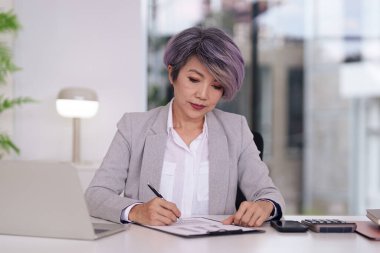 Asyalı kadın profesyonel, kaliteli bir ofis ortamında, gerekli evrak işleriyle ilgilenir. Şirket operasyonları için belgeler imzalandı.