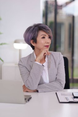 Masasında derin düşüncelere dalmış deneyimli bir Asyalı iş adamı. Gözlüklerini yeni kavramları ve kariyer fırsatlarını düşünürken tutuyor..