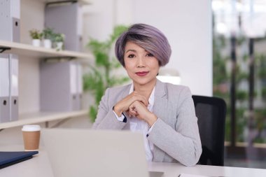 Başarılı Asyalı kadın profesyonel yönetici ofis masasında otururken kendine güven ve deneyim saçar..