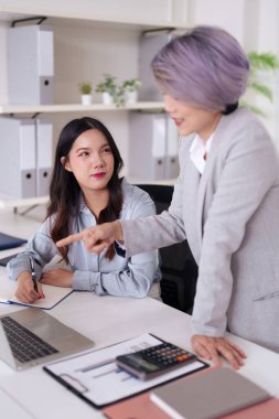 Profesyonel Asyalı kadınlar modern bir ofiste birlikte çalışırlar. Bir akıl hocası genç bir meslektaşına büyüme ve takım çalışmasını teşvik eden iş stratejileri konusunda rehberlik eder. Kurumsal eğitim ve geliştirme için ideal.