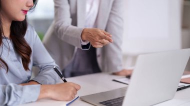 Profesyonel Asyalı kadın modern bir ofiste not almayı öğreniyor. Deneyimli meslektaş, ortak bir iş görüşmesi sırasında rehberlik eder.