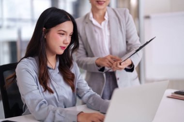 Parlak bir ofiste işbirliği yapan profesyonel Asyalı kadınlar. Yetişkin bir akıl hocası genç bir işçiye modern bir dizüstü bilgisayar ile rehberlik eder..
