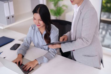 İki Asyalı kadın aktif olarak profesyonel ofis işi yapıyor. Bir son sınıf öğrencisi, etkili proje işbirliği için başka bir teknolojiden yararlanmayı öneriyor.