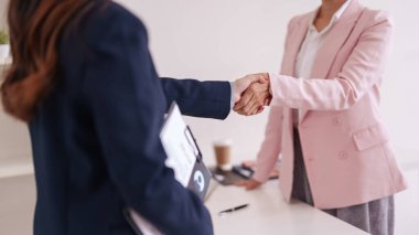 İki yetişkin Asyalı kadın, güven ve işbirliği sinyalleri veren parlak çağdaş bir ofiste sıkı bir tokalaşmayla profesyonel anlaşmayı sonuçlandırdı.