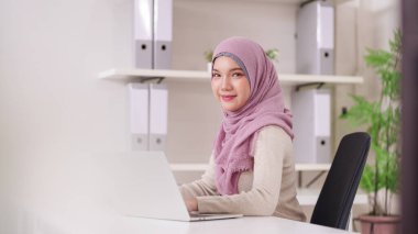 Kendine güvenen genç Asyalı Müslüman kadın profesyonel olarak bilgisayarını büyümeyi ve hırsı teşvik eden çağdaş bir ofiste etkili bir şekilde çalıştırıyor..