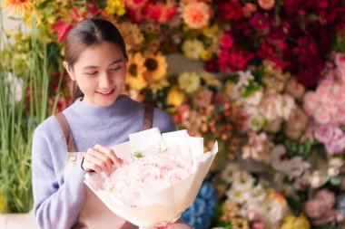 Genç Asyalı çiçekçi, hayat dolu çiçekçisinde sersemletici pembe bir gül buketi düzenliyor. Neşeli, profesyonel, taze çiçekler hazırlıyor.
