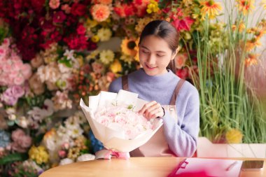 Genç Asyalı çiçekçi taze pembe gül buketini ustalıkla düzenliyor. Nazik elleri, canlı çiçekçi dükkanında büyüleyici bir çiçek deseni oluşturuyor. Mükemmel bir hediye.