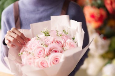 Asyalı çiçekçi ellerini nazikçe tut canlı pembe gül buketi damlaları görünür çiçekçi dükkanının arka planında taze yapraklar