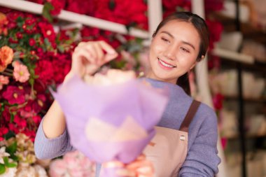 Gülümseyen Asyalı kadın çiçekçi büyüleyici perakende dükkanında renkli bir çiçek buketi düzenliyor güzel çiçek tasarımları yapıyor.