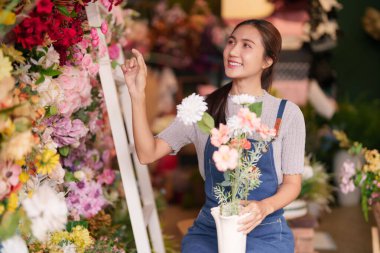 Neşeli Asyalı kadın, canlı çiçekçisinde titizlikle taze çiçekler düzenler. Müşteriler için canlı çiçekler üretir.