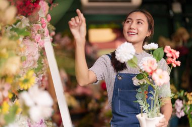 Gülümseyen Asyalı kadın çiçekçi canlı bir perakende dükkanında güzel çiçekler düzenliyor. Neşeli işi hoş müşteri deneyimleri yaratıyor..