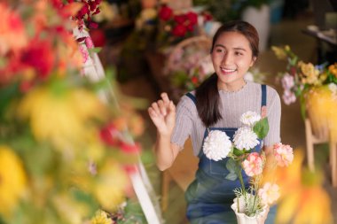 Gülümseyen Asyalı genç yetişkin kadın renkli çiçekleri ustalıkla seçiyor. Çiçek aranjmanları sunuyor. Neşe ve doğa bağlantısını teşvik ediyor..