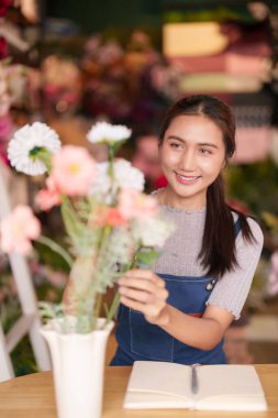 Gülümseyen Asyalı çiçekçi canlı çiçekler düzenler güzel tasarımlar yaratır. Müşteriler için zarif çiçek düzenlemeleri hazırlıyor.