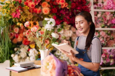 Çalışkan bir Asyalı kadın çiçekçi çiçek tasarımı fikirlerini kaydeder ve çiçekçi dükkanında iş siparişlerini yönetir..