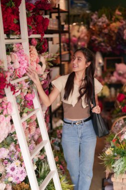 Gülümseyen Asyalı kadın büyüleyici bir çiçekçide taze çiçeklerle meşgul oluyor. Çok canlı bir çiçek aranjmanı buluyor..