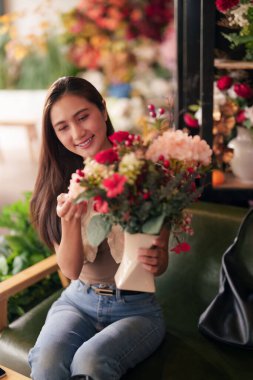 Gülümseyen Asyalı kadın canlı bir çiçekçi stüdyosunda çarpıcı çiçek düzenlemeleri yapıyor. Renkli taze çiçekleri ve yeşil yaprakları idare ediyor. Çiçek işi ya da yaşam tarzı içeriği için mükemmel.