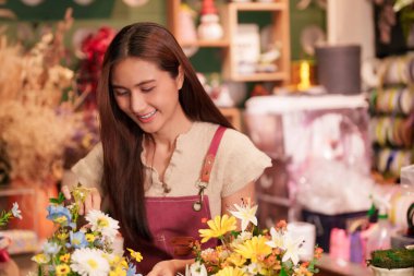 Genç Asyalı kadın sanatsal çiçek desenleri tasarlıyor. O, canlı buketler ustaca el sanatları yapar. Onun neşeli ifadesi çiçekçiliğe olan tutkuyu vurguluyor. Bu resim adanmışlığı ve yaratıcılığı yakalar..