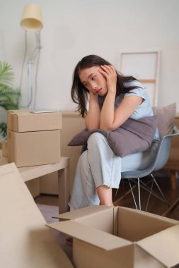 Genç Asyalı kadın kutuları taşırken üzgün hissediyor. Taşınma ve ev geçişi onu bunaltıyor. Bu görüntü duygusal gerginliği gösteriyor.