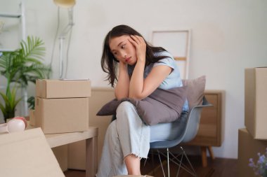 Yetişkin Asyalı kadın, taşınma yolculuğu sırasında etrafı karton kutularla çevrili olduğu için stresli ve bitkin hissediyor.