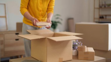 Kadın özenle taşınmaya hazırlanıyor. Kişisel eşyaları karton kutulara koyuyor. Bu organize taşınma işlemi ile yeni bir bölüm başlıyor.