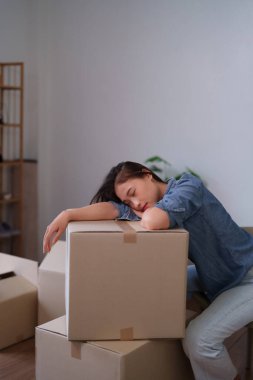 Taşındıktan sonra tamamen yıpranmış hisseden genç bir Asyalı kadın yeni yaşam alanındaki eşyalarının üzerinde yatıyor.