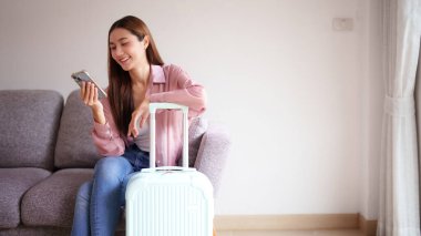 Gülümseyen kadın seyahat planları hazırlıyor telefondaki mobil uygulama bavulun yanında heyecanlı bir sonraki macera tatiline hazır