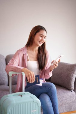 Mutlu Asyalı kadın heyecan verici uluslararası seyahatler planlıyor. Elinde pasaport ve eve dönüş bileti olan akıllı bir telefon kullanıyor..