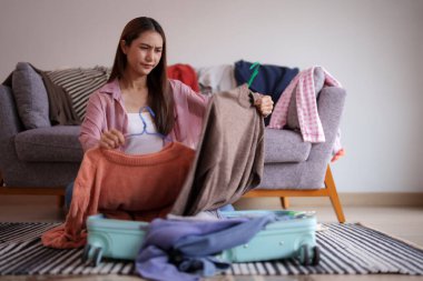 Genç bir kadın, yolculuğu için kıyafet seçerken bavul hazırlamakla karşı karşıya. Macera planlaması için giysileri titizlikle bavula koyuyor..