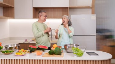 Neşeli Asyalı yaşlılar çağdaş mutfaklarında sağlıklı yemekler hazırlamaktan hoşlanırlar. Bu mutlu çift spatula ile şarkı söylüyor, neşeli bir aile ortamı yaratıyor..