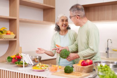 Asyalı yaşlı yetişkinler sağlıklı yemek için taze sebzeler hazırlıyorlar modern mutfak mutlu gülümseyen çift evde birlikte yemek pişirmekten zevk alıyor.