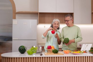 Mutlu Asyalı yaşlı çift modern bir ev mutfağında taze sebze ve meyve hazırlıyor. Birlikte sağlıklı yemek yapmayı seviyorlar..