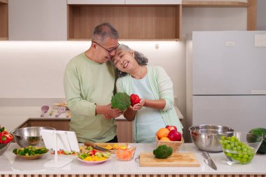 Mutlu Asyalı yaşlı yetişkinler sağlıklı yiyecekler hazırlar. Taze sebzelerin tadını çıkar. Modern mutfak sahnesi refahı ve birlikteliği resmediyor..