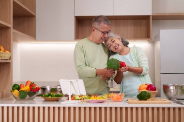 Neşeli Asyalı son sınıf çifti, çağdaş mutfaklarında besleyici taze sebzeler hazırlıyor. Mutluluğu paylaşmak sağlıklı yemek pişirme tarzı.